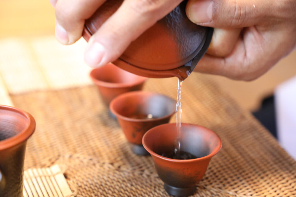 急須から複数の湯飲みにお茶を注ぐ手元