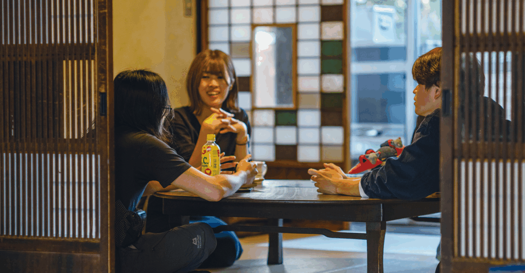室内のテーブルを囲んで話す3人